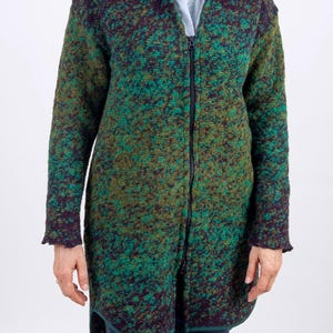 May include: A long, textured cardigan in shades of green, purple, and brown. The sweater has a full-length zip and long sleeves with ruffled cuffs. The garment appears to be made of a thick, warm material, suitable for cooler weather.