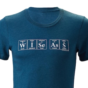 Puede incluir: Una camiseta azul turquesa con un gr&aacute;fico blanco de la tabla peri&oacute;dica de los elementos que deletrea la palabra "WISE".