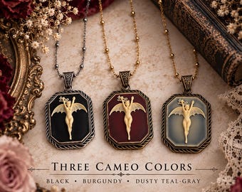 May include: Three necklaces featuring rectangular pendants with a cream-colored winged figure relief. The pendants come in black, burgundy, and dusty teal-gray. Each hangs from a beaded chain. Text reads: THREE CAMEO COLORS BLACK BURGUNDY DUSTY TEAL-GRAY.