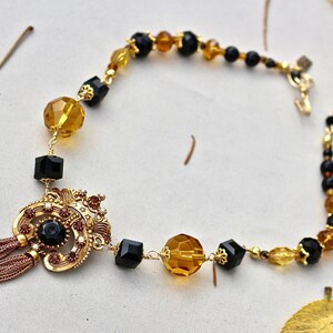 May include: A gold necklace with a black and amber bead design. The necklace features a gold pendant with a black stone and a tassel.