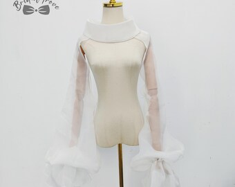 May include: A white, sheer bridal bolero with a high, rounded collar and long, voluminous sleeves. The sleeves gather at the wrists, creating a ruffled effect. The bolero is displayed on a mannequin. The logo "Bridal Trove" is visible in the upper left corner.