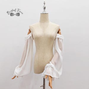 May include: White off-the-shoulder sleeves with long, flowing fabric and ruffled cuffs. The sleeves are displayed on a mannequin. The text "Bridal Trove" is in the upper left corner.