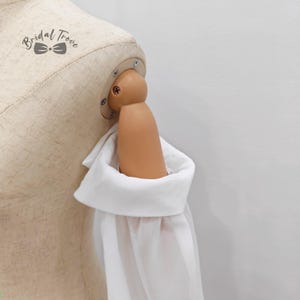 May include: A white long-sleeve shirt with a wide cuff is displayed on a mannequin. The mannequin's arm is visible, and the shirt's cuff is folded over. The background is a plain white wall. The text "Bridal Trove" is visible.