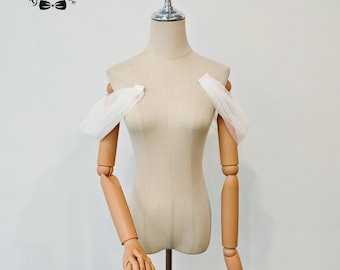 May include: A beige dress form with articulated wooden arms and hands. The dress form has a metal stand and is adorned with white fabric sleeves. The logo "Bridal Trove" is visible in the upper left corner.