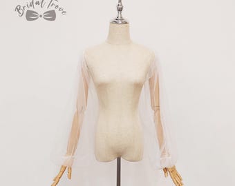 May include: A sheer white bridal sleeve overlay with long, billowy sleeves and fitted cuffs. The overlay is draped over a mannequin, showcasing its delicate, airy fabric. The Bridal Trove logo is visible in the upper left corner.