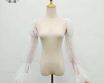 May include: White tulle sleeves with ruffled cuffs and gathered details, displayed on a mannequin. The sleeves have a romantic, flowing design, perfect for bridal or formal wear. The mannequin has a gold-colored top.