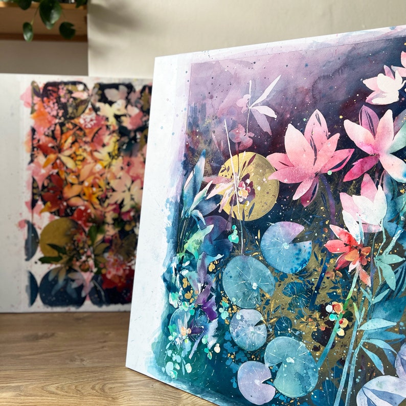 May include: Watercolor painting of a floral scene with pink water lilies, green lily pads, and gold accents on a dark blue background.