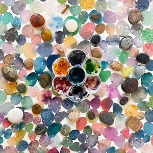 以下が含まれることがあります： パステルカラーの重なり合う円のパターンが特徴的な水彩画。さまざまな色と質感の小さな滑らかな小石が表面に散らばっています。さまざまな色で満たされた花型のペイントパレットが中央にあります。