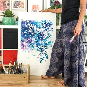 May include: An abstract watercolor painting with a vibrant display of blues, purples, and white. The artwork features a dynamic composition of layered brushstrokes and splatters, creating a sense of depth and movement. The painting is displayed on a white canvas.