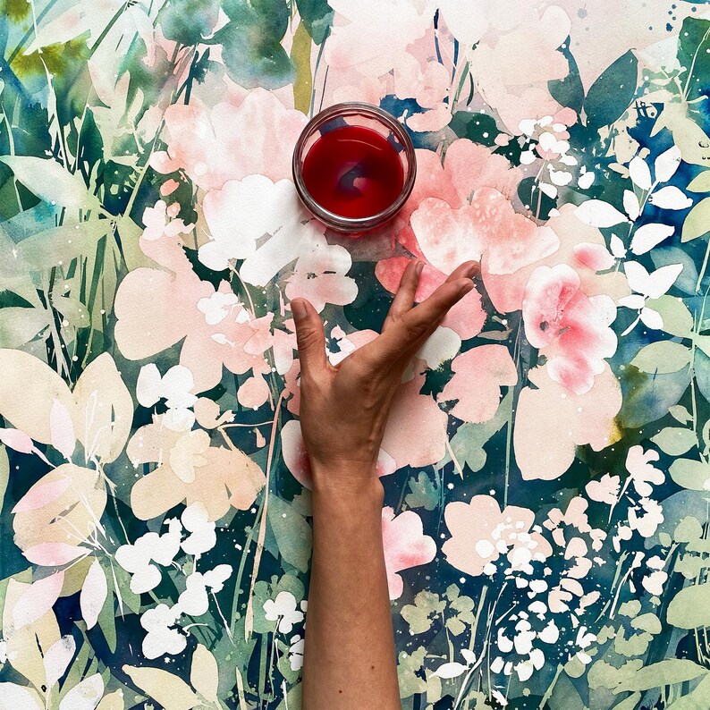 Op de afbeelding: Een heldere glazen kom gevuld met een dieprode vloeistof, geplaatst op een bloemige aquarelachtergrond. De achtergrond toont roze en witte bloemen met groene bladeren. Een hand reikt naar de kom.