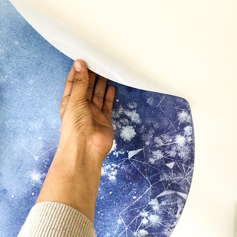 May include: A close-up of a blue and white patterned wallpaper being applied to a wall. The wallpaper features a watercolour-like design with white stars and geometric shapes on a blue background.