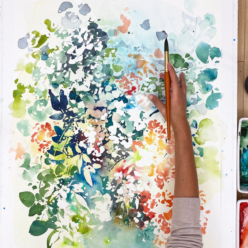 May include: A watercolor painting of a floral bouquet with a brush and hand holding the brush. The flowers are painted in shades of red, orange, yellow, green, and blue. The background is white.