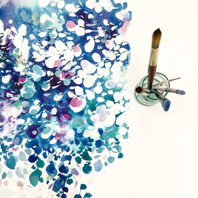 May include: An abstract watercolor painting with a floral theme, featuring a blend of blue, white, teal, and purple hues. Several paint brushes are arranged in a small glass jar, suggesting an art studio setting.
