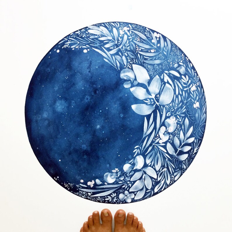 Puede incluir: Una pintura de acuarela azul de una luna creciente con dise&ntilde;os florales blancos. La luna est&aacute; pintada sobre un fondo blanco.