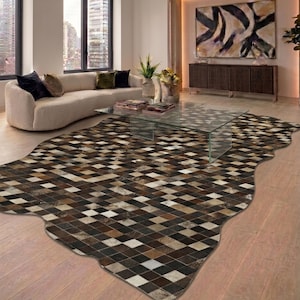 May include: A large, irregularly shaped rug with a geometric pattern of brown, tan, and cream-coloured squares. The rug is placed on a light-coloured hardwood floor in a modern living room. A glass coffee table sits on top of the rug.