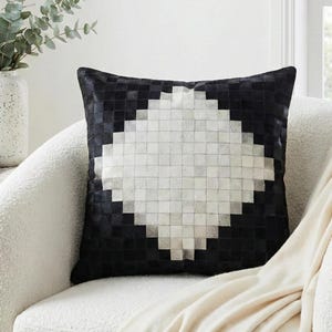 Könnte beinhalten: Ein quadratisches Zierkissen mit einem Patchwork-Design aus kleinen schwarzen und weißen Lederquadraten. Das Muster ist so angeordnet, dass es eine große weiße Rautenform bildet, die sich von einem schwarzen Hintergrund abhebt.