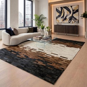 May include: A rectangular rug with a geometric pattern in black, brown, and white. The rug is made of rectangular pieces arranged in horizontal bands. The rug is placed in a modern living room setting with a sofa and coffee table.