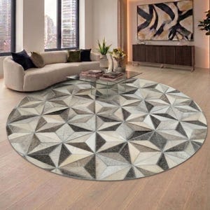 May include: A large circular area rug featuring a geometric pattern of triangles in shades of white, gray, and dark charcoal. The rug is constructed from individual panels with a textured surface, creating a three-dimensional visual effect.