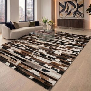 Könnte beinhalten: Ein rechteckiger Teppich mit einem Patchwork-Design. Der Teppich hat abwechselnde horizontale Streifen in Braun, Schwarz, Weiß und Beige. Der Teppich liegt auf einem hellen Parkettboden in einem Wohnzimmer.