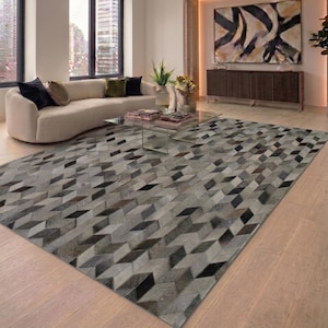 Peut inclure: Un tapis rectangulaire présentant un motif géométrique répétitif de cubes en trois dimensions. Le tapis est composé de pièces individuelles de cuir poilu dans des tons variés de gris, noir, blanc et marron, créant une surface texturée.