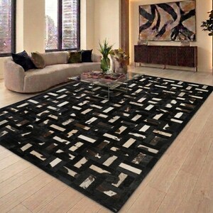 Peut inclure: Un tapis rectangulaire présentant un motif géométrique en vannerie, composé de pièces individuelles en peau de vache. Le tapis affiche une palette de couleurs contrastées composée de noir uni, de blanc et de tons bruns tachetés.