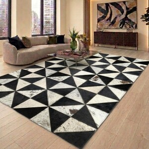Puede incluir: Una alfombra rectangular con un patrón geométrico de triángulos negros y blancos alternos. La alfombra está construida con paneles de piel de vaca cosidos, mostrando variaciones naturales en la textura y el color en toda la superficie.