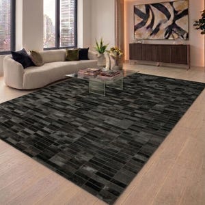 Könnte beinhalten: Ein großer, rechteckiger Teppich mit einem geometrischen Muster aus schwarzen und grauen rechteckigen Formen. Der Teppich liegt auf einem hellen Holzboden in einem modernen Wohnzimmer. Der Raum verfügt außerdem über ein weißes Sofa, einen Glastisch und Kunstwerke.