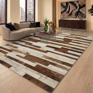 Peut inclure: Un tapis rectangulaire composé d'un assemblage de pièces de peau de vache dans des tons variés de brun, de beige et de crème. Le tapis est formé de bandes rectangulaires disposées selon un motif linéaire, créant une surface texturée avec des coutures visibles.