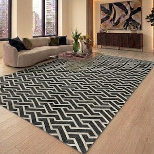 May include: A rectangular area rug featuring a repeating geometric pattern in black and white. The design consists of interlocking lines that create a continuous zigzag effect across the entire surface of the floor covering.