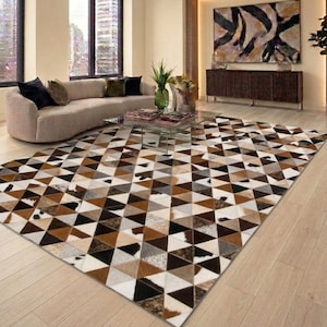 Puede incluir: Una alfombra rectangular grande con un patrón geométrico compuesto por piezas triangulares. La alfombra muestra una mezcla de tonos marrones, negros, blancos y grises con texturas variadas, creando un diseño de patchwork en toda la superficie.