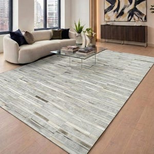 Könnte beinhalten: Ein rechteckiger Teppich mit einem Patchwork-Design aus horizontalen Streifen in verschiedenen Grau-, Weiß- und Beigetönen. Der Teppich besteht aus mehreren rechteckigen Segmenten, die in einem linearen Muster angeordnet sind.