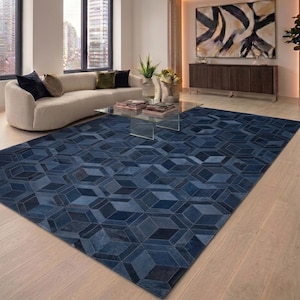 May include: A large, geometric patterned rug in shades of blue dominates the room. The rug's design features a repeating pattern of three-dimensional shapes. The rug is placed on a light-colored hardwood floor, complementing the room's modern aesthetic.