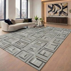 Puede incluir: Una alfombra rectangular grande con un patrón geométrico de cuadrados entrelazados en tonos gris, blanco y carbón. La alfombra está construida con paneles texturizados dispuestos para crear un efecto visual tridimensional en el suelo.