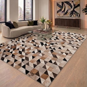 May include: A rectangular area rug featuring a geometric pattern of triangles in shades of brown, black, and beige. The rug is laid on a light wooden floor in a modern living room. The design of the rug provides a contemporary aesthetic to the room.