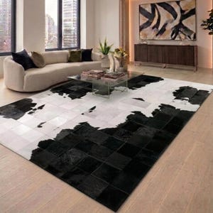 Puede incluir: Una alfombra rectangular con un diseño de mosaico compuesto por cuadrados negros y blancos. La alfombra presenta un patrón de alto contraste con secciones sólidas en negro y blanco, creando una estética geométrica inspirada en piel de vaca.