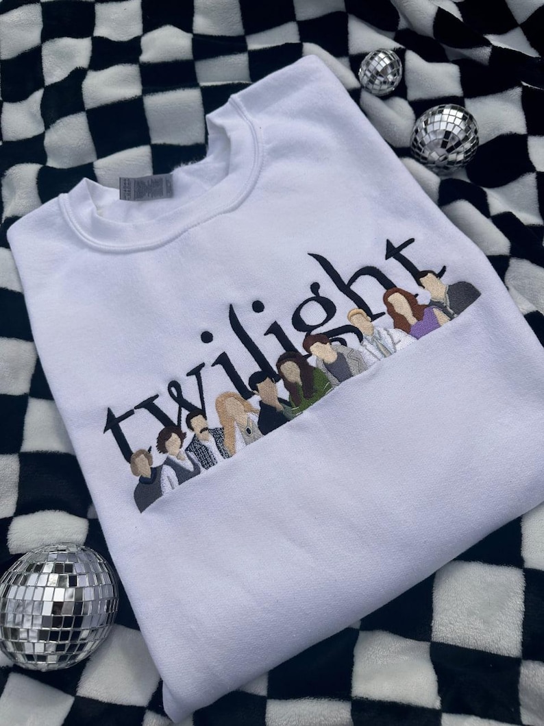 May include: White sweatshirt with the word "Twilight" embroidered in black, with a line of character illustrations below. The sweatshirt is made of a soft material. The background is a black and white checkered pattern.
