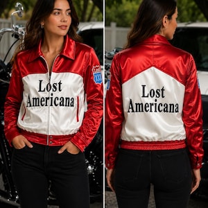 May include: A red and white satin bomber jacket featuring a collar, long sleeves, and a front zipper closure. The text "Lost Americana" is printed in black on the white chest and back panels. A blue shield patch with "Lost" and "XXX" is on the sleeve.