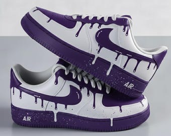 Può includere: Due scarpe da ginnastica bianche e viola con un design a goccia. Le scarpe da ginnastica hanno una base bianca con dettagli viola, tra cui il logo Nike e la suola. La parola "AIR" è stampata sul lato.