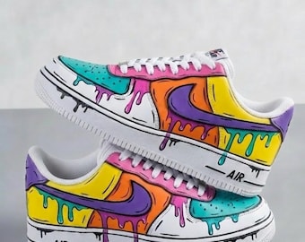 May include: Two white sneakers with colorful paint drip designs. The shoes feature a white base with teal, pink, orange, yellow, and purple accents. The Nike swoosh is purple. The word "AIR" is printed on the side of the sole.