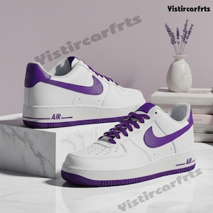 Könnte beinhalten: Weiße und lila Sportschuhe mit dem Wort "AIR" auf der Seite. Die Schuhe haben ein lila Swoosh-Logo und lila Schnürsenkel. Die Schuhe werden auf einer weißen Marmoroberfläche präsentiert.