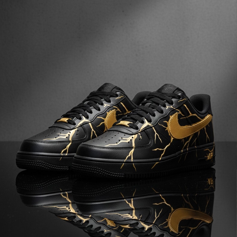 May include: Pair of black sneakers with gold lightning bolt designs and gold swoosh logos. The shoes have black laces and soles. The word "AIR" is visible on the side of the shoe.