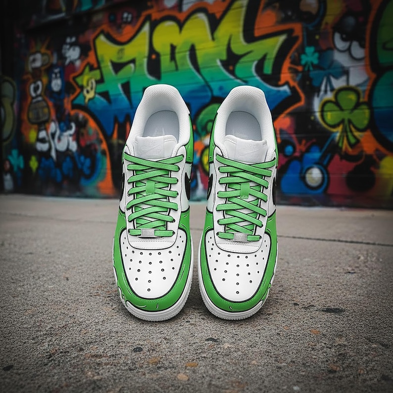 Puede incluir: Un par de zapatillas blancas y verdes con cordones verdes. Las zapatillas tienen una base blanca con detalles verdes y un logotipo de swoosh negro. Las zapatillas est&aacute;n sobre un fondo de graffiti colorido.