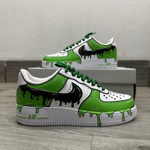 Puede incluir: Zapatillas personalizadas blancas y verdes con detalles en negro. Las zapatillas presentan un dise&ntilde;o de goteo verde y negro en la parte superior e intermedia de cuero blanco. El logo de Nike es negro. Cordones verdes.