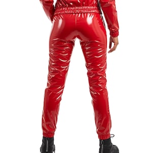 K&ouml;nnte beinhalten: Ein gl&auml;nzender roter Vinyl-Overall. Das Outfit umfasst eine Jacke und eine Hose. Die Hose hat einen gerafften Kn&ouml;chel und eine gl&auml;nzende, reflektierende Oberfl&auml;che. Das Model tr&auml;gt schwarze Stiefel.