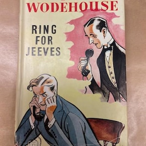 May include: Vintage hardcover book titled "Ring for Jeeves" by P.G. Wodehouse. The cover features illustrations of two men on the phone, one in a suit and the other in a tuxedo. The book has a cream-colored background with red and pink accents.