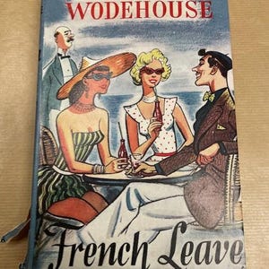 May include: Vintage paperback book titled "French Leave" by P.G. Wodehouse. The cover art depicts a seaside scene with three people at a table, a waiter, and the ocean in the background. The cover is blue with red and white accents.