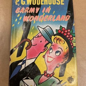 May include: Vintage paperback book titled "Barmy in Wonderland" by P.G. Wodehouse. The cover features a colorful illustration of two cartoon characters, a man with a hat and a woman with a berry-adorned headband, against a yellow and blue background.