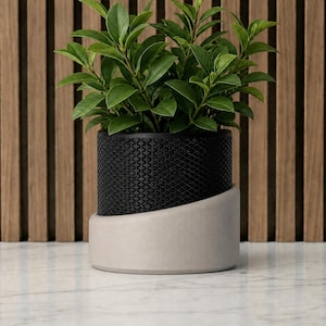 May include: A potted plant with vibrant green leaves sits in a black textured pot, resting on a light gray, curved base. The plant pot is set against a backdrop of vertical wooden slats.