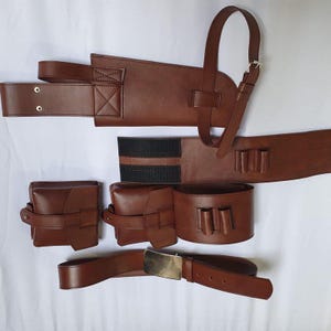 May include: A brown leather utility belt set, featuring a belt with a rectangular buckle, two pouches, a holster, and a bandolier-style strap. The set includes a belt with a rectangular buckle, two pouches, a holster, and a bandolier-style strap.