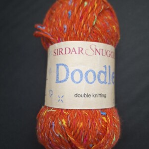 May include: A ball of orange Sirdar Snuggle Doodle double knitting yarn. The yarn has flecks of blue, yellow, and pink. The label reads "Sirdar Snuggle Doodle" in blue script.